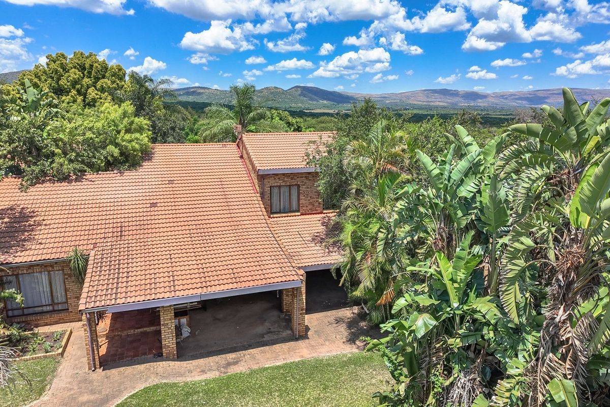 Aerial view of a brick farmhouse with a terracotta tile roof, featuring a covered patio and expansive surrounding landscape.
