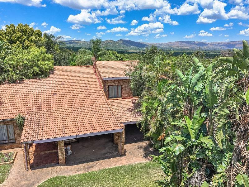 Aerial view of a brick farmhouse with a terracotta tile roof, featuring a covered patio and expansive surrounding landscape.