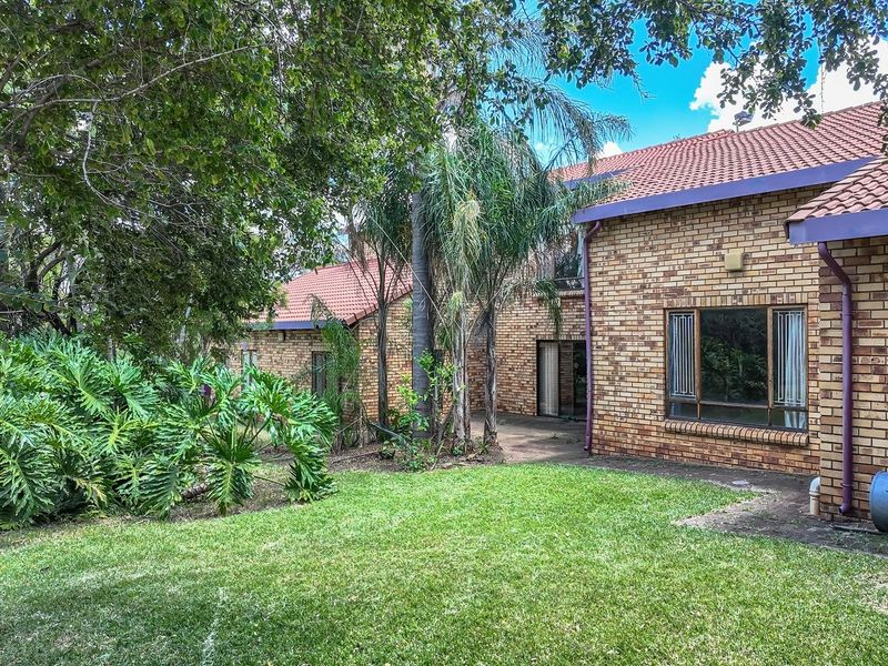 Rear view of a face brick farmhouse featuring a tiled roof, concrete patio area, and established garden surroundings.