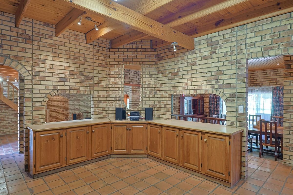 Spacious living area featuring rustic face brick walls, exposed timber ceiling beams, terracotta floor tiles, and extensive built-in timber cabinetry with arched architectural details.
