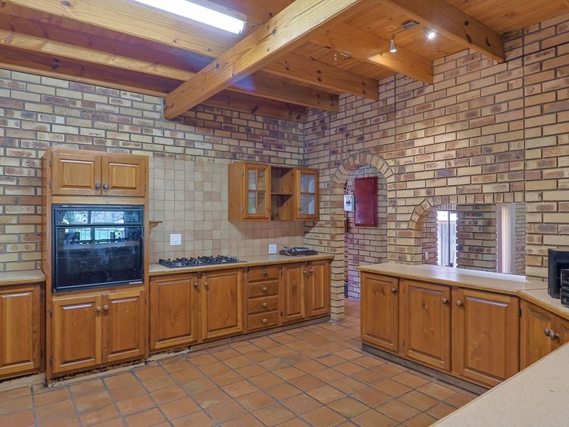 Rustic kitchen featuring exposed timber beams, face brick walls, terracotta flooring, and traditional wooden cabinetry with a built-in oven and gas hob.