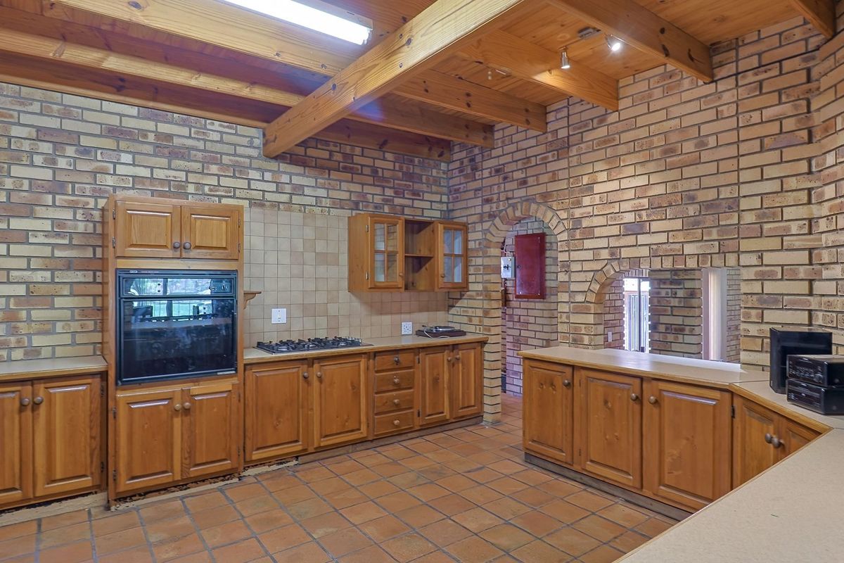 Rustic kitchen featuring exposed timber beams, face brick walls, terracotta flooring, and traditional wooden cabinetry with a built-in oven and gas hob.