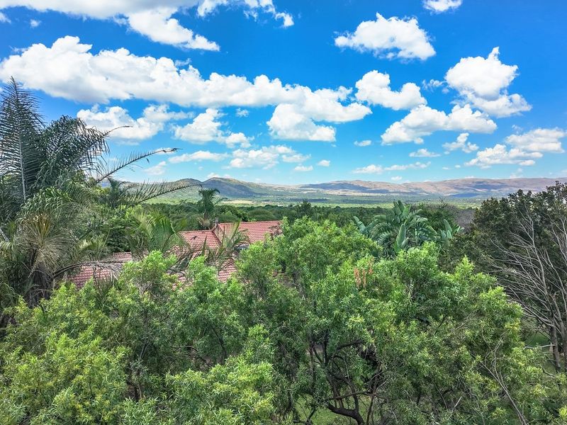 A scenic elevated view overlooking the lush green landscape and surrounding hills, featuring a glimpse of the property's terracotta tiled roof.
