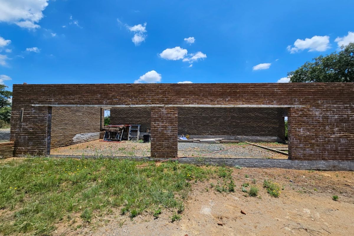 An exterior view of a property under construction, featuring exposed brick walls and an unfinished foundation structure.