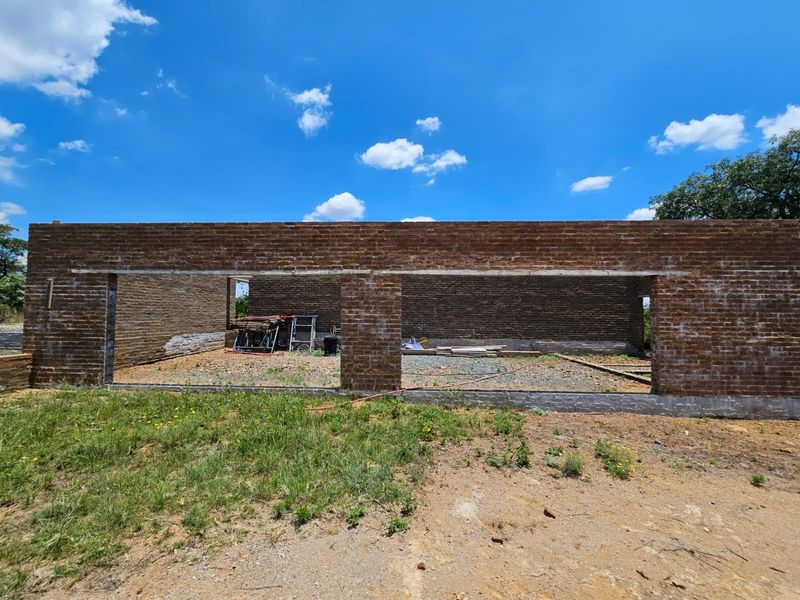 An exterior view of a property under construction, featuring exposed brick walls and an unfinished foundation structure.