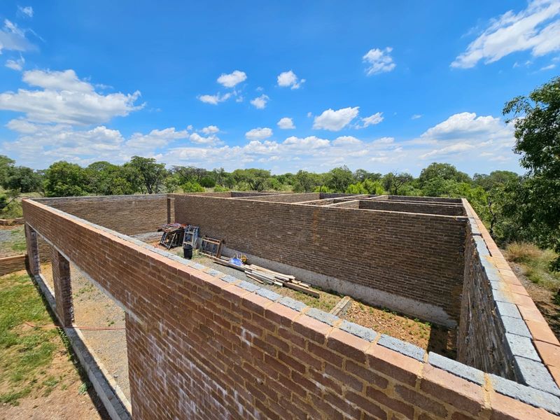 An aerial view of a property under construction, showing the exposed brick wall structure and foundation layout on a large plot.