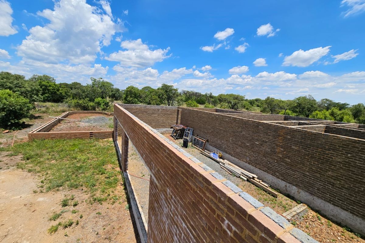 An elevated view of a property under construction, showing exposed brick walls and foundation work in a rural setting.