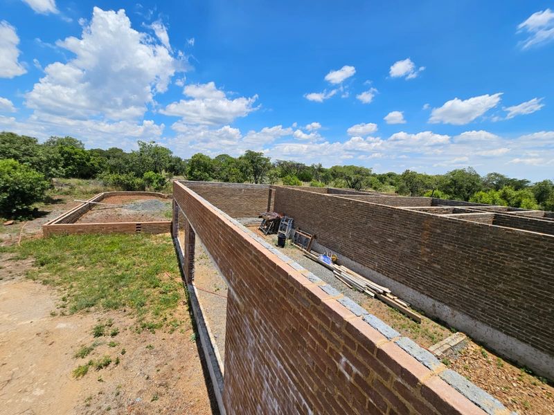 An elevated view of a property under construction, showing exposed brick walls and foundation work in a rural setting.