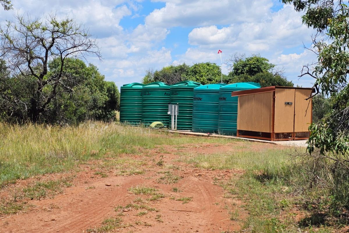 Outdoor utility area featuring multiple large green water storage tanks and a dedicated pump house structure on a concrete base.