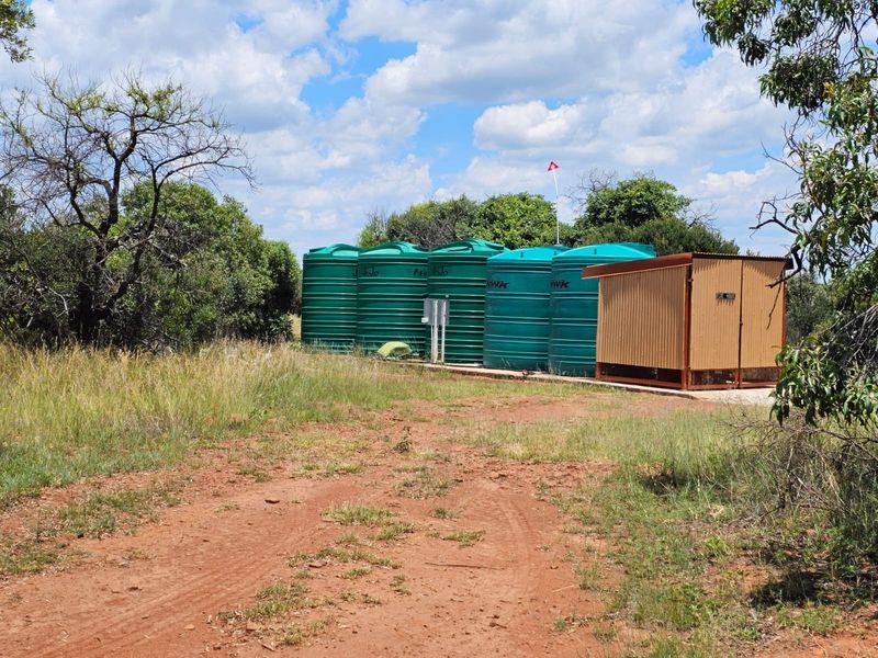 Outdoor utility area featuring multiple large green water storage tanks and a dedicated pump house structure on a concrete base.