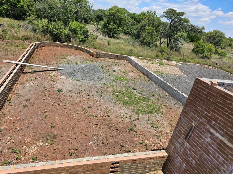 An elevated view of an unfinished rear yard area featuring brick retaining walls and a gravel-prepared foundation base.