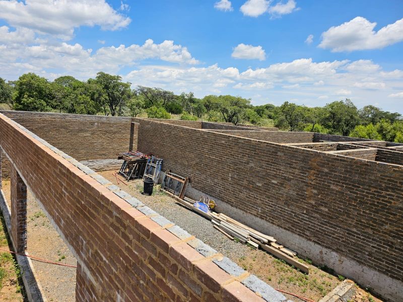 An aerial view of a property under construction, showing exposed brick walls and an unfinished layout set against a natural landscape.