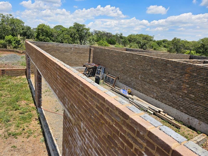 An elevated view of a property under construction, showing exposed brick walls and structural framing in a rural setting.