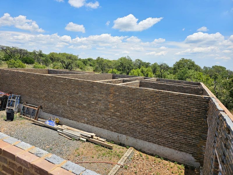 An elevated view of a property under construction, showing the brick masonry walls and foundation layout in a rural setting.
