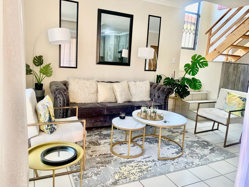 A well-lit living room featuring tiled flooring and an open staircase with a wooden handrail, creating a bright and inviting atmosphere.