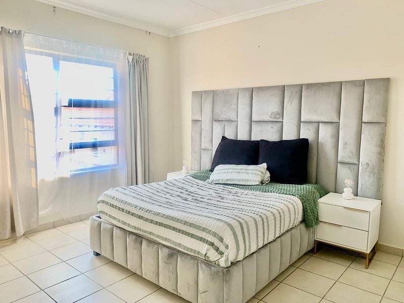 A well-lit bedroom featuring neutral tiled flooring, coved ceiling details, and a large window providing natural light.