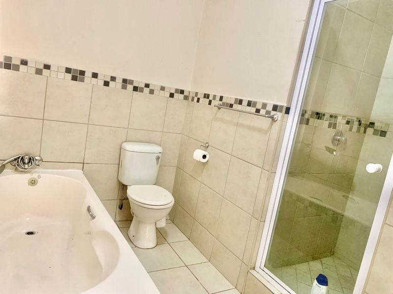 A functional bathroom featuring a bathtub, a separate shower enclosure with glass door, and neutral wall and floor tiling.
