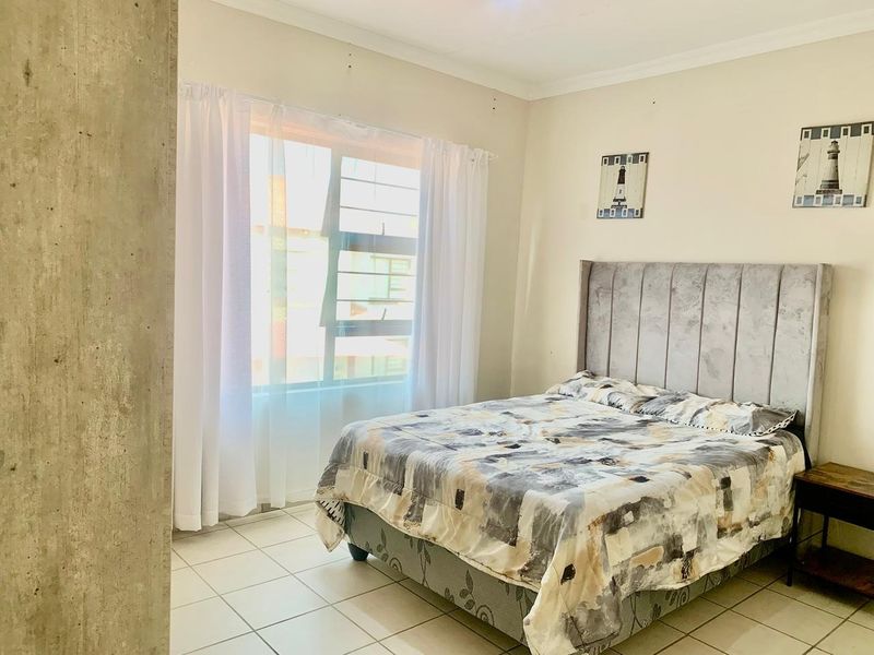 A functional bedroom featuring tiled flooring and a large window, providing natural light and a neutral foundation for personal styling.