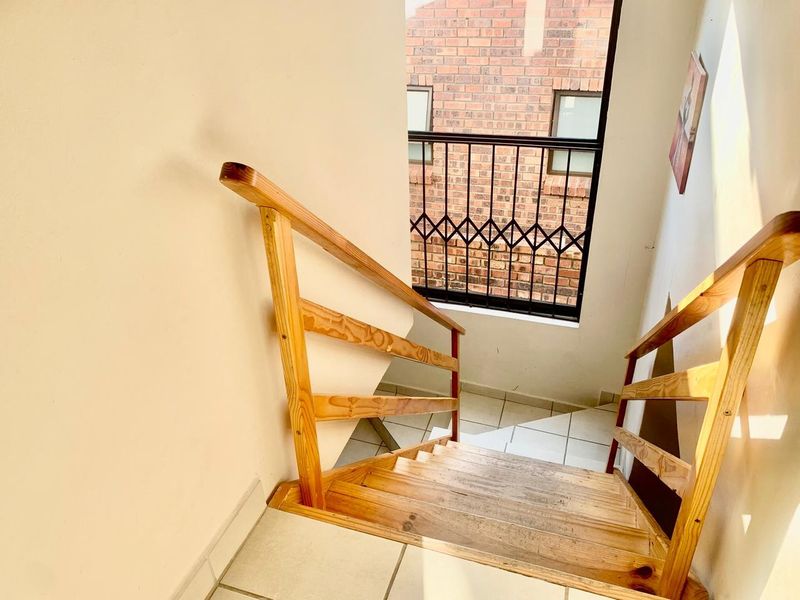 A staircase featuring wooden steps and handrails, leading to a landing with a security gate and tiled flooring.