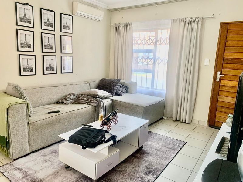 A comfortable living room featuring tiled flooring, a wall-mounted air conditioning unit, and a window fitted with a security gate.