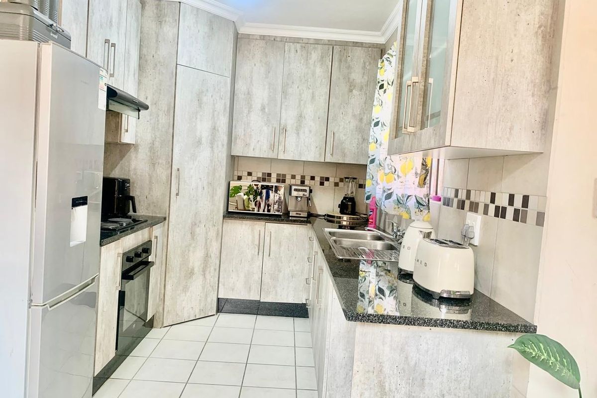 A functional kitchen featuring light wood-grain cabinetry, granite countertops, a stainless steel sink, and built-in oven with extractor fan.