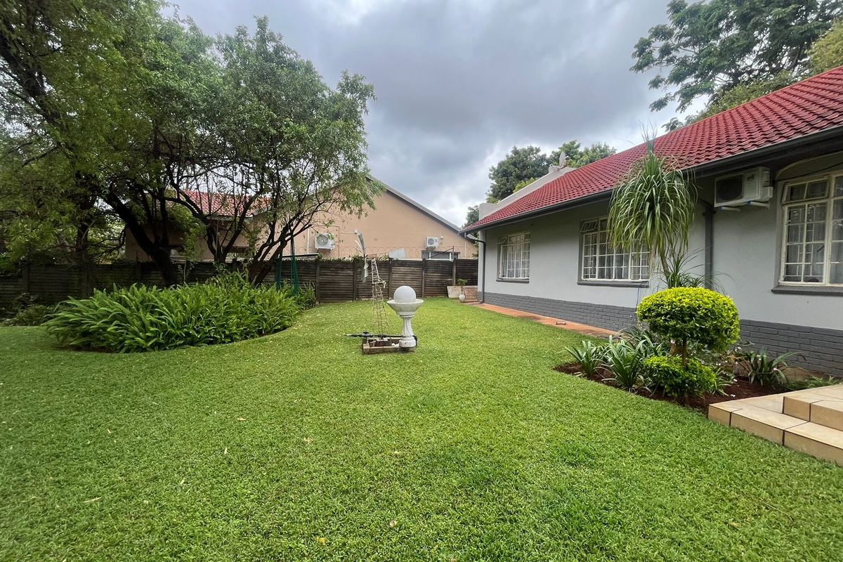 A well-maintained rear garden featuring a lush lawn, established landscaping, and a clear view of the property's rear brick facade and tiled roof.