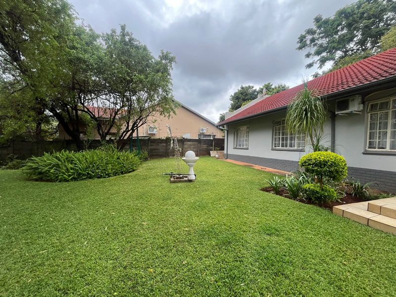 A well-maintained rear garden featuring a lush lawn, established landscaping, and a clear view of the property's rear brick facade and tiled roof.