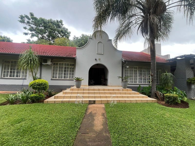 Front elevation of a traditional house featuring a prominent arched entrance, tiled steps, and a red tile roof set within a landscaped garden.