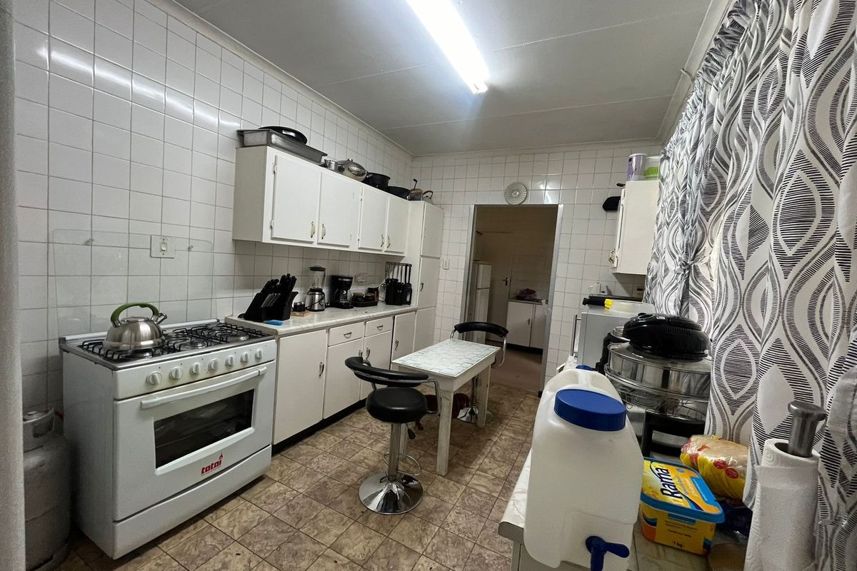 A functional kitchen featuring white cabinetry, a gas stove, and full-height wall tiling, offering a practical layout with potential for modern updates.