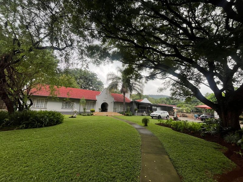 A well-maintained single-story residence featuring a classic gabled roof, a paved walkway, and expansive landscaped gardens under mature trees.