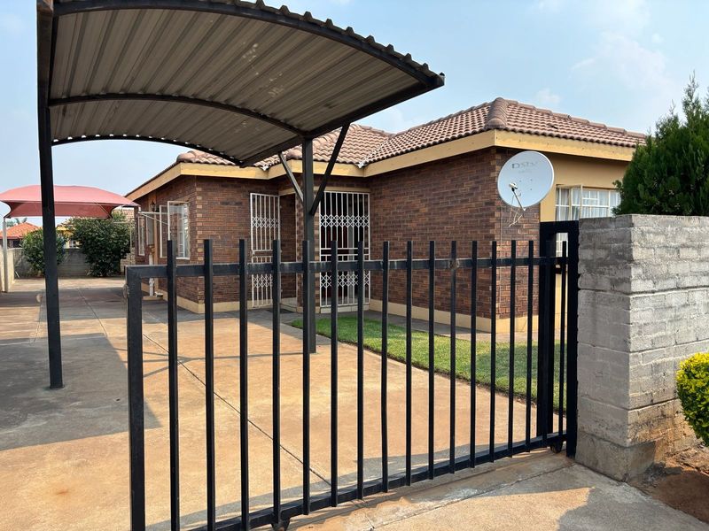 Front view of a brick house featuring a paved driveway, covered carport, and secure gated entrance with security bars on windows.