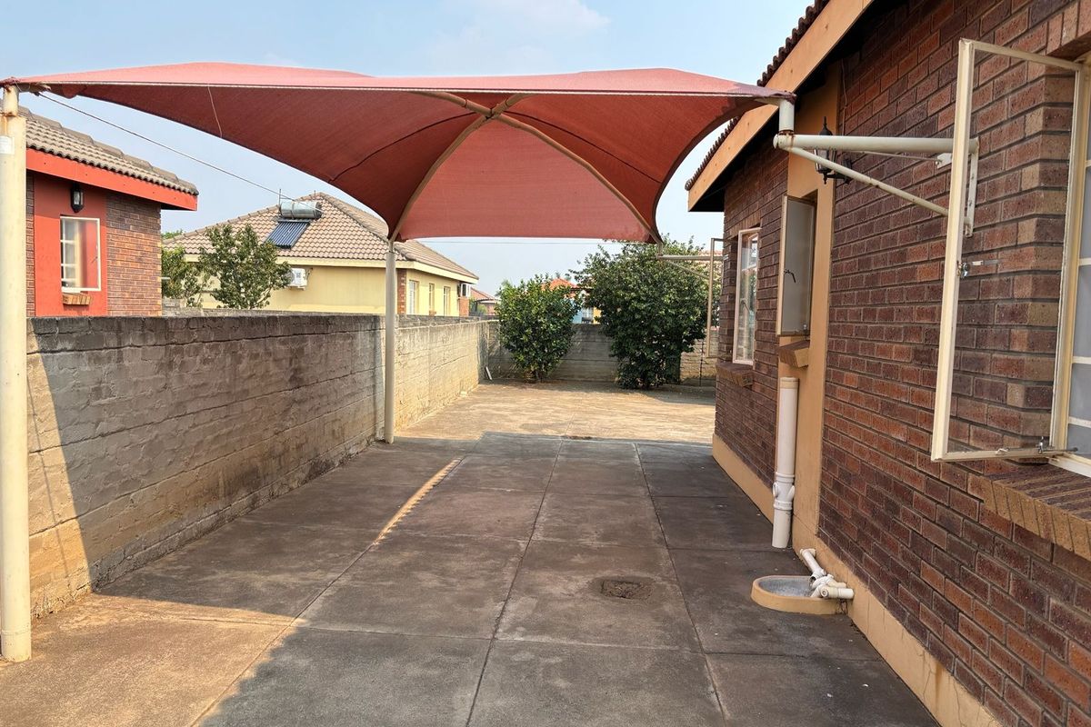 Rear exterior area featuring concrete paving, a brick boundary wall, and a shade sail structure attached to the face brick house.
