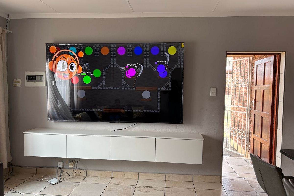 Living room featuring ceramic floor tiles, a wall-mounted media console, and direct access to an exterior area through a security gate and timber door.