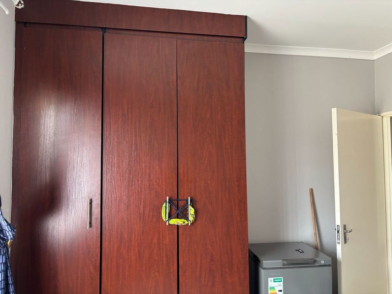 A bedroom featuring a large, dark wood-finish built-in wardrobe with integrated storage and standard internal door access.