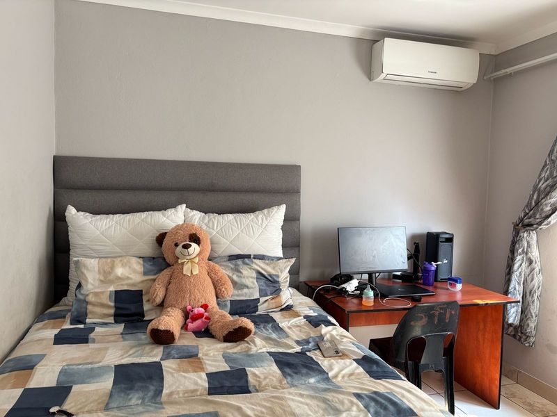 A functional bedroom featuring a wall-mounted air conditioning unit, tiled flooring, and an upholstered headboard, providing a comfortable and practical living space.