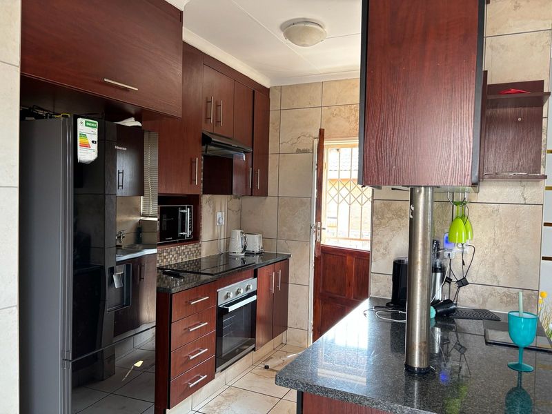 A functional kitchen featuring dark wood cabinetry, granite countertops, built-in oven and hob, and tiled finishes with direct access to the exterior.