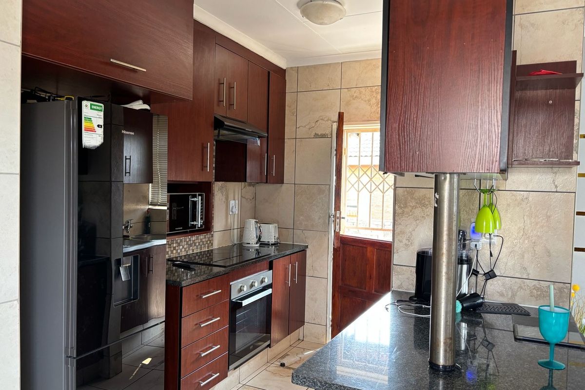 A functional kitchen featuring dark wood cabinetry, granite countertops, built-in oven and hob, and tiled finishes with direct access to the exterior.