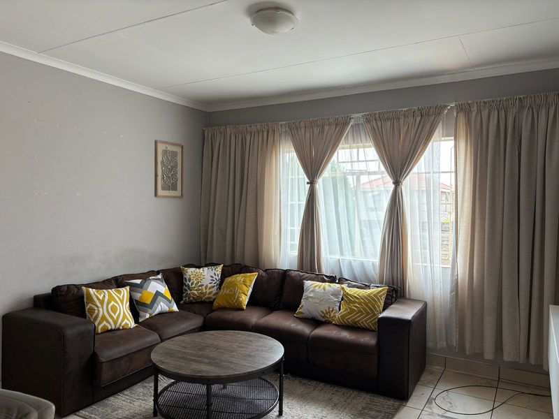 A living room featuring tiled flooring, neutral wall tones, and a large window with security bars, providing a functional and comfortable living space.