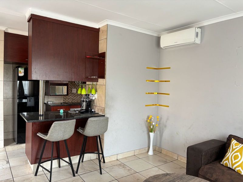 Open-plan living area featuring a kitchen with dark wood cabinetry, granite countertops, breakfast bar, and a wall-mounted air conditioning unit.