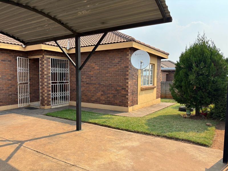 A well-maintained face brick house exterior featuring a covered carport, security gates, and a neat garden area.