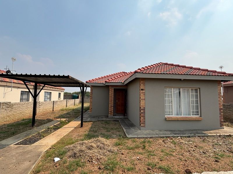 Front view of a single-story house featuring a tiled roof, brick accents, and an attached carport with a concrete walkway.
