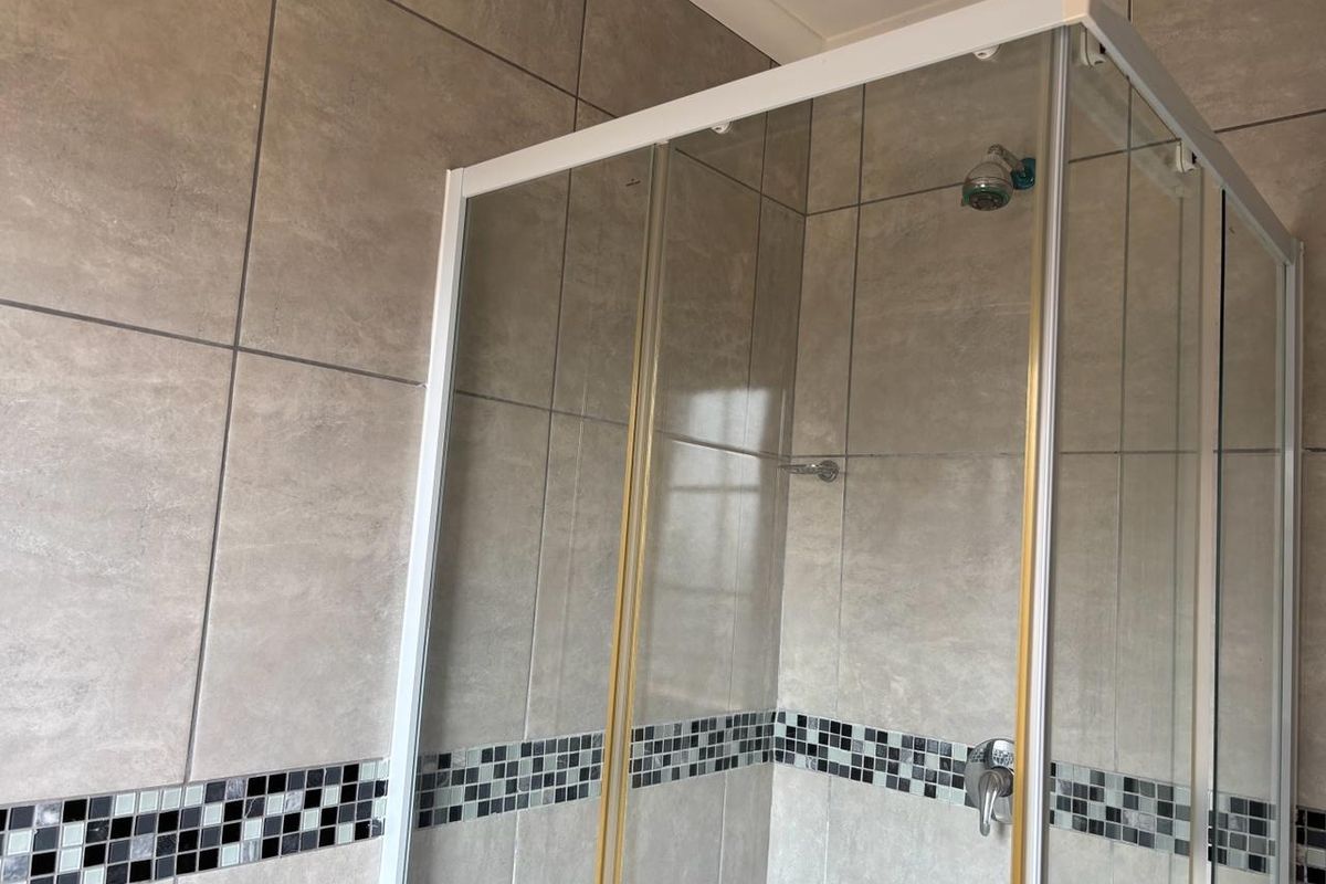 A clean bathroom shower enclosure featuring neutral large-format wall tiles with a decorative black and white mosaic border.