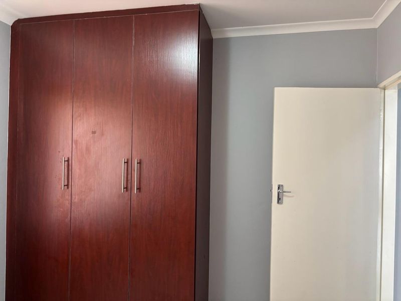 A bedroom interior featuring a dark wood-finish built-in wardrobe and a standard internal door.