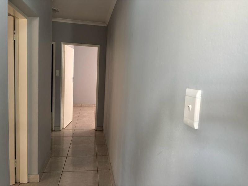 A clean, neutral-toned hallway featuring tiled flooring and simple architectural finishes, providing access to adjacent rooms.