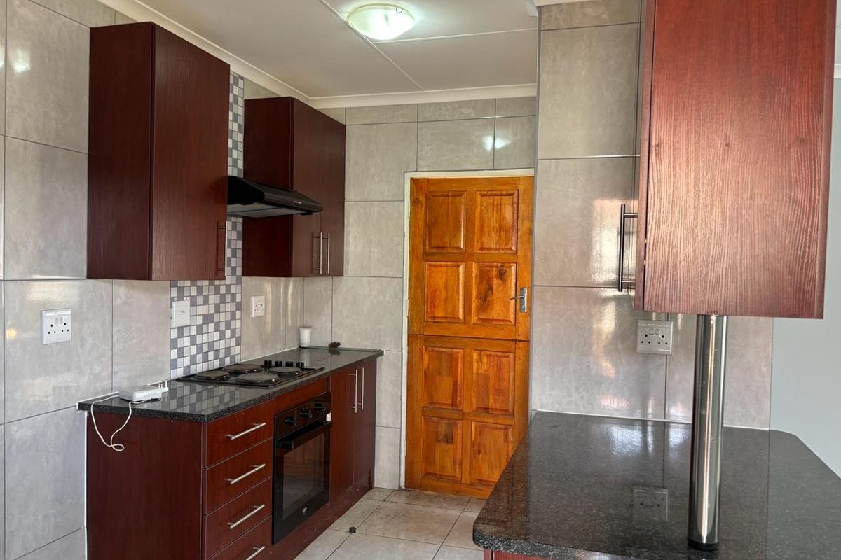 A functional kitchen featuring dark wood cabinetry, granite countertops, built-in oven and hob, and neutral wall tiling.