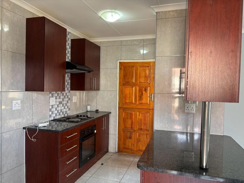 A functional kitchen featuring dark wood cabinetry, granite countertops, built-in oven and hob, and neutral wall tiling.