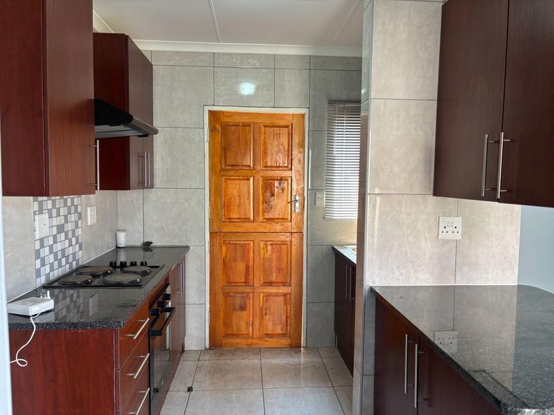 A functional kitchen featuring dark wood cabinetry, granite countertops, built-in oven and hob, and a classic timber stable door leading to the exterior.