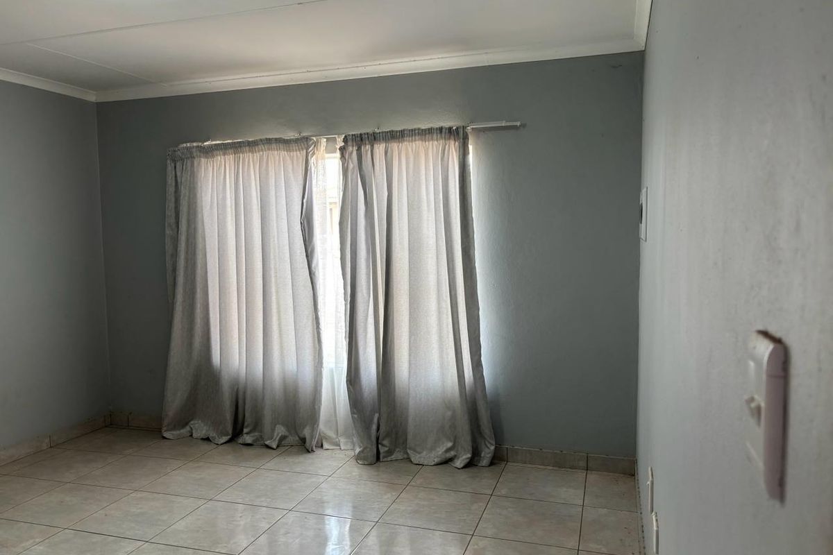A vacant bedroom featuring neutral grey walls, tiled flooring, and installed curtain rails, providing a blank canvas for personalization.