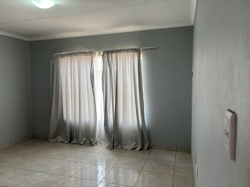 A vacant bedroom featuring neutral grey walls, tiled flooring, and installed curtain rails, providing a blank canvas for personalization.