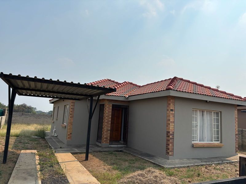 Front view of a single-story house featuring a tiled roof, brick accents, and a covered carport area with a concrete driveway.